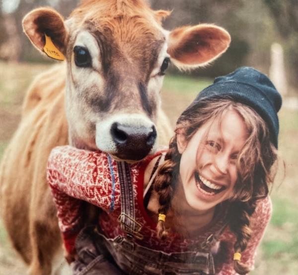 A photograph of Nellie Geraghty laughing with a cow behind her resting it's head on her shoulder
