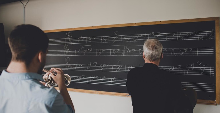Student playing trumpet, teacher at chalkboard